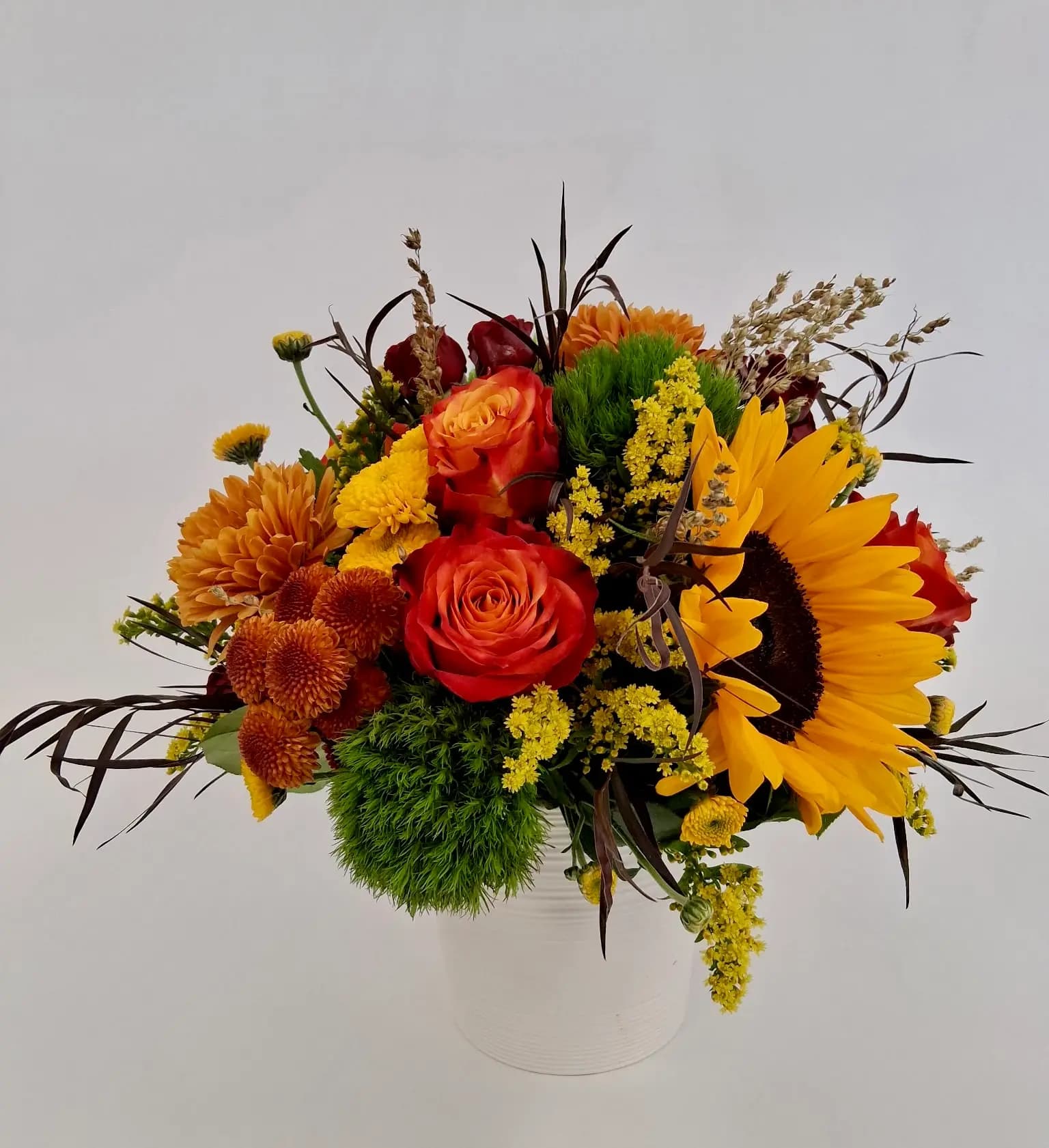 1 sunflower, 3 orange/yellow roses, 2 chrysanthmum and 2 green dianthus in a ceramic vase