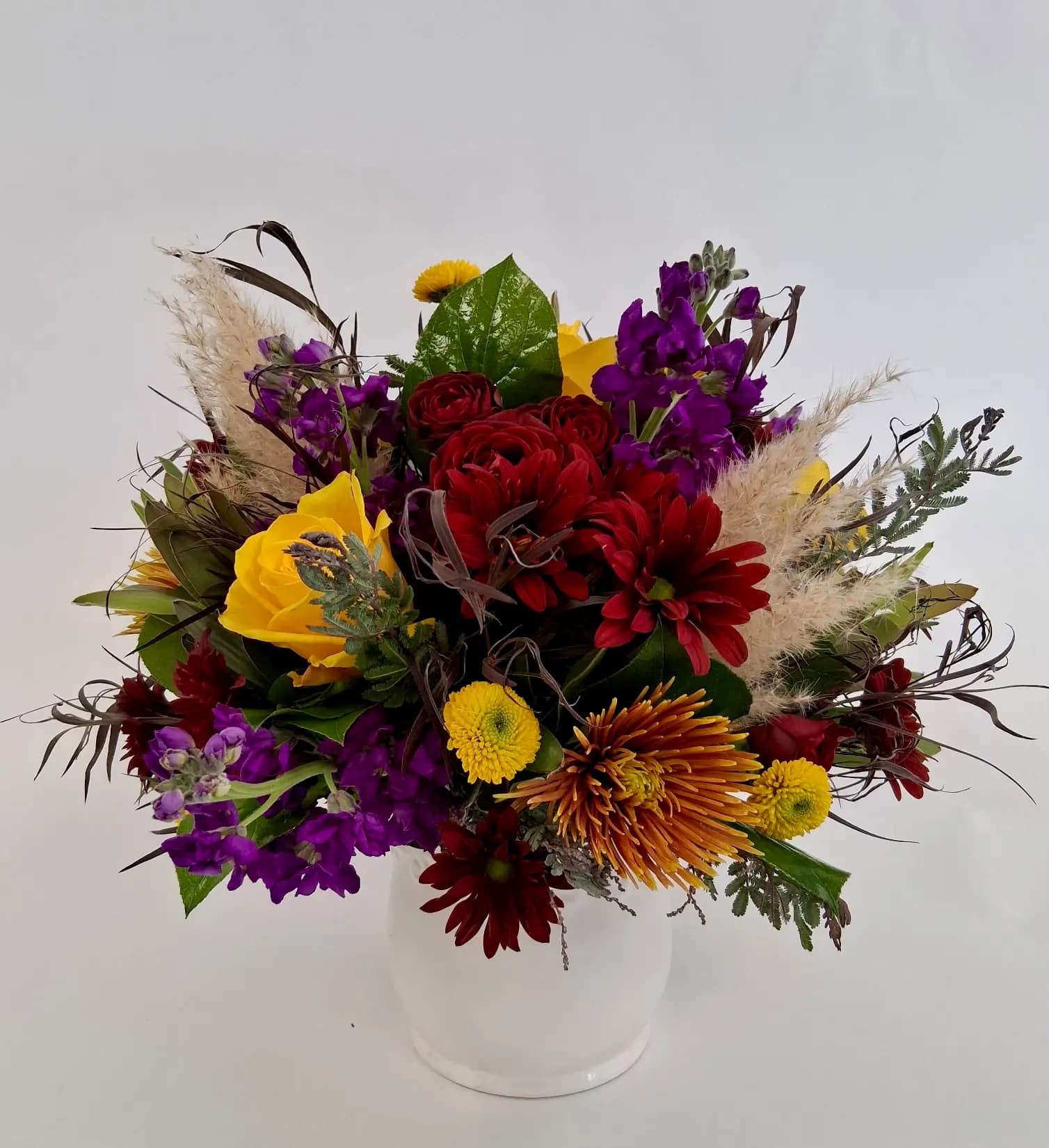 yellow roses, yellow button mums, red daisies, purple stock, red spray roses, orange chrysanthemums