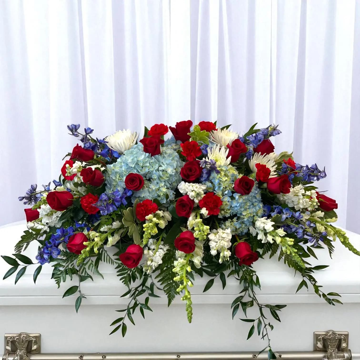 Patriotic casket spray with red roses, white hydrangea, and blue delphinium